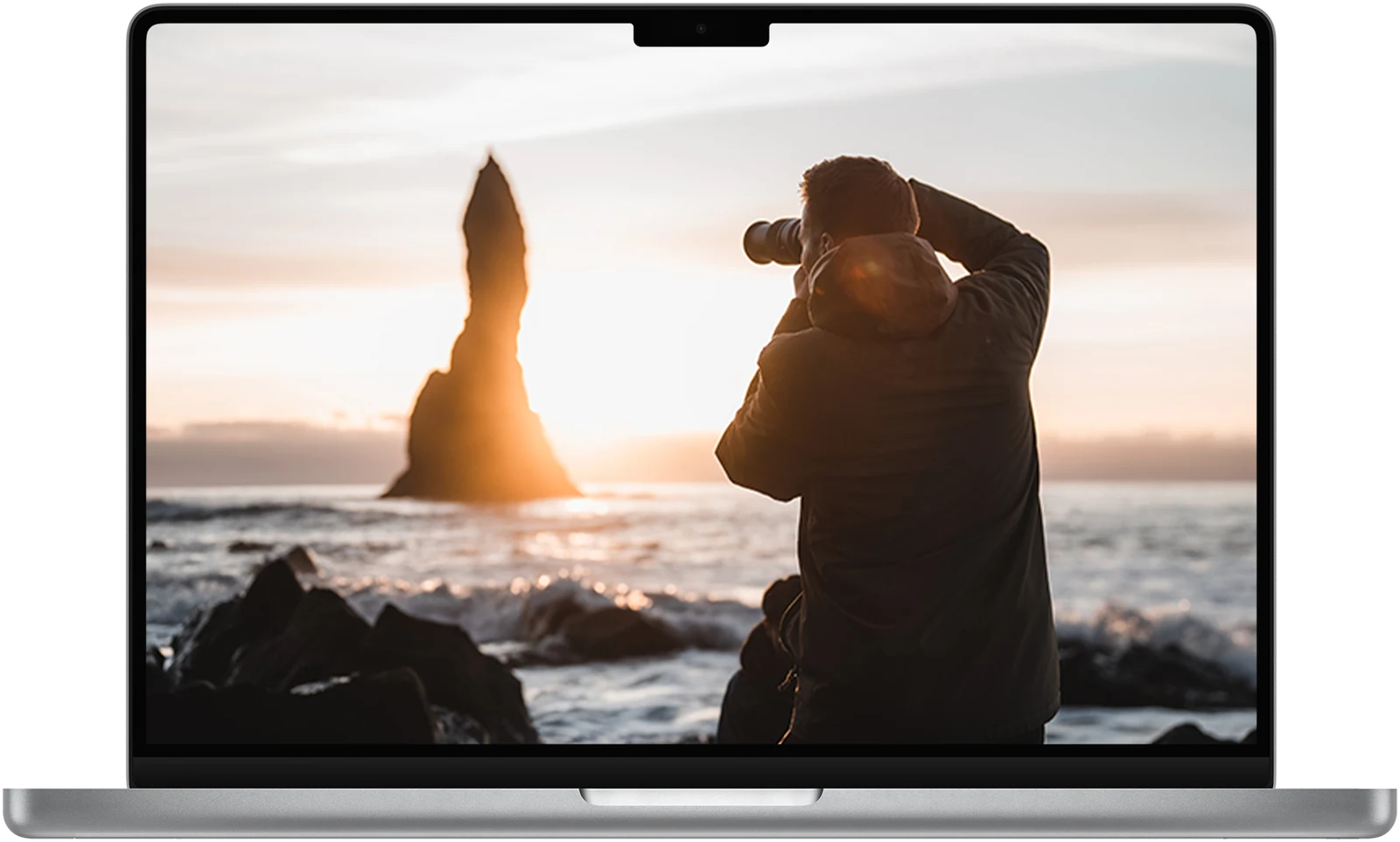 Feedback Area in Creator Community Nederland: een laptop met daarop een fotograaf met een lange lens op een zwart zandstrand bij zonsondergang, met een hoge rots in zee
